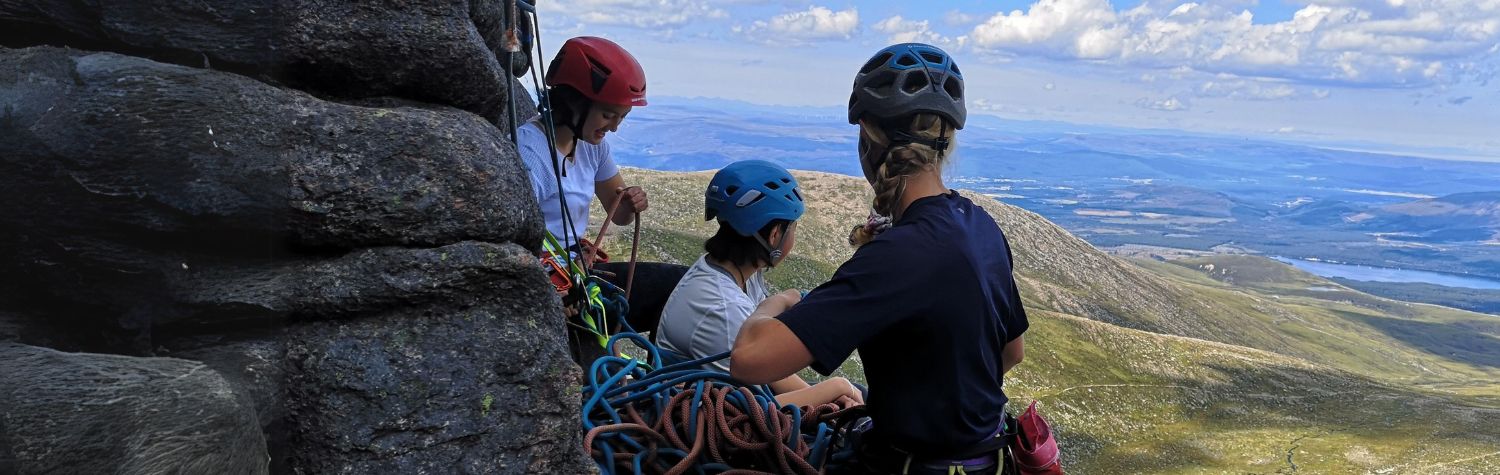 Two young girls trad climbing in the mountains with a female instructor