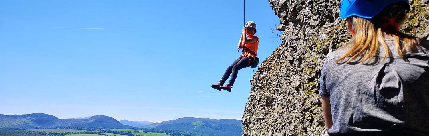 A young person being lowered off a rock face during a climbing session.