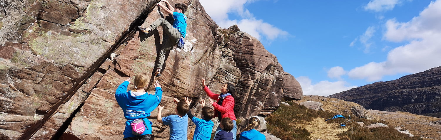 A group of people watching someone bouldering on a rock.