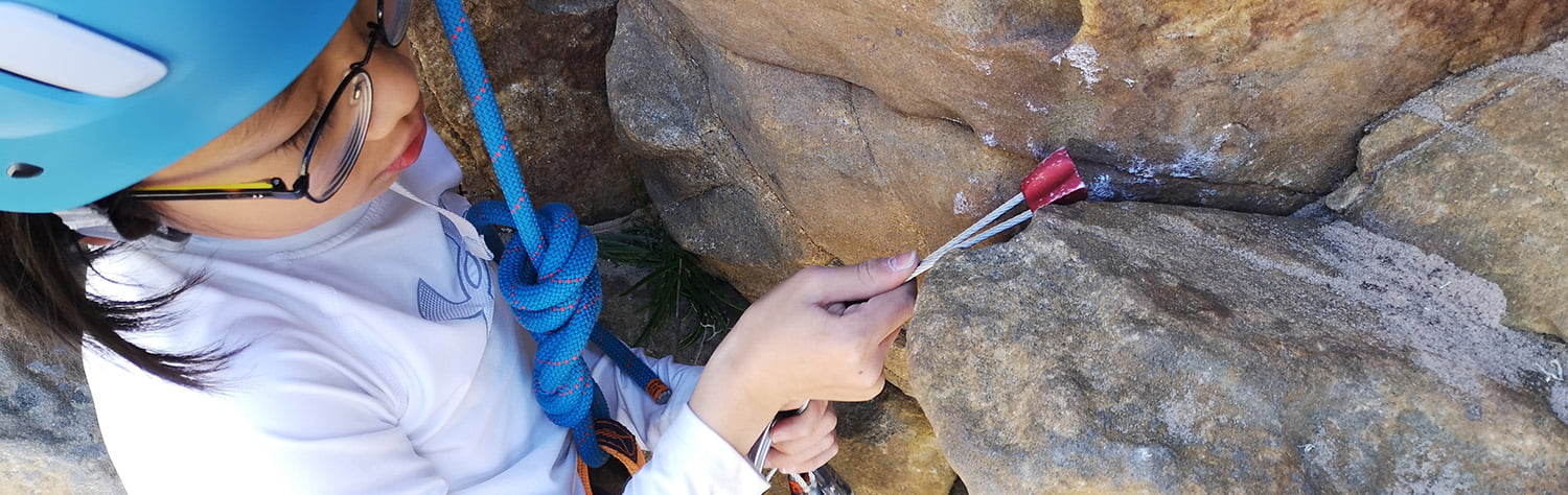 A young girl placing a bit of climbing gear into a rock.